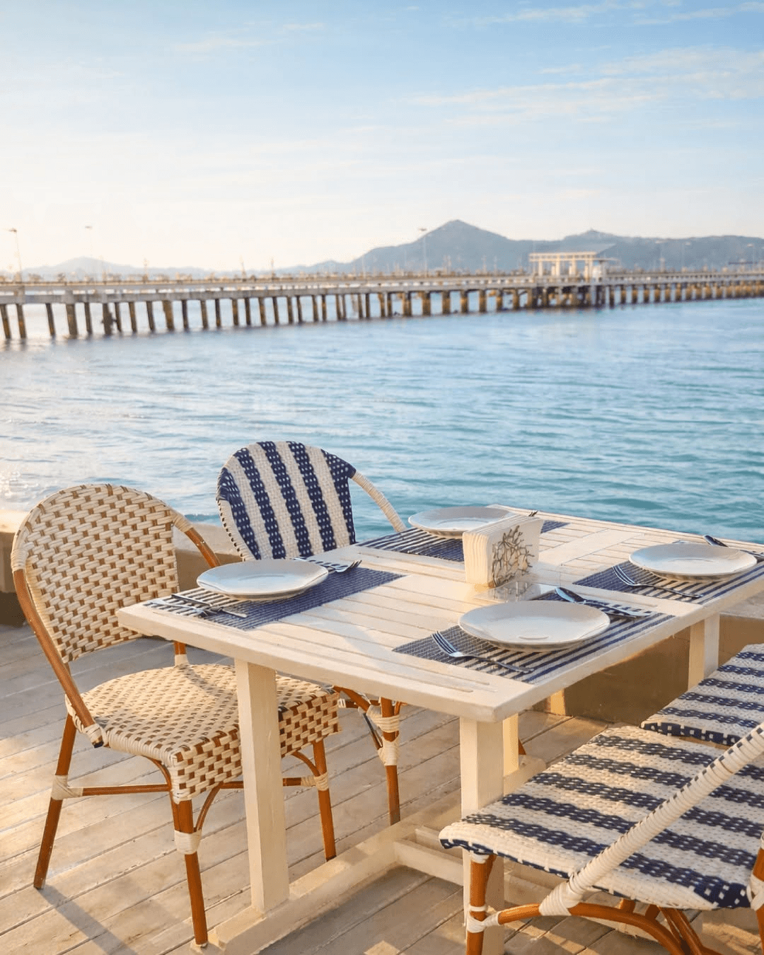 A white dining table with blue woven chairs beside Chalong Pier