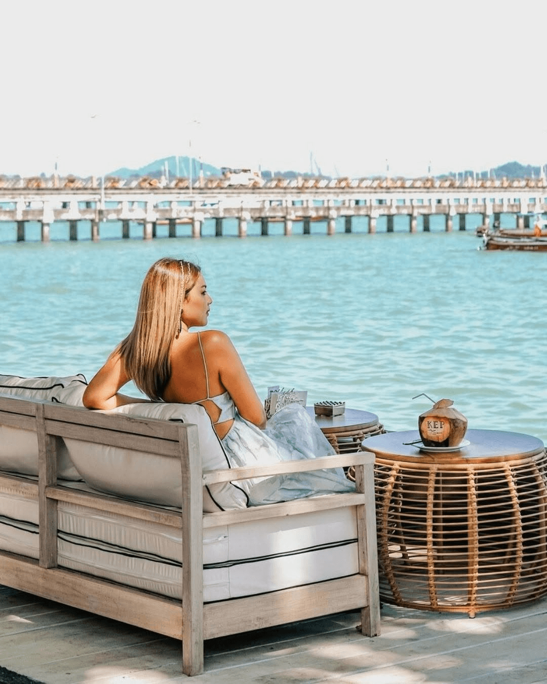A guest relaxing on a waterfront sofa with a fresh coconut at KEP